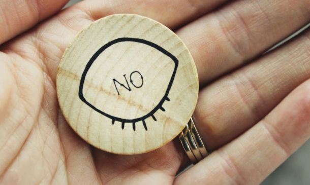 Hand holding a brown wood ornament that says NO