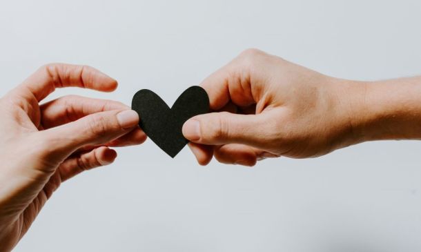 Two hands holding a black heart paper cut out