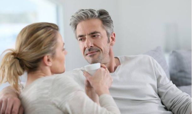 Middle aged couple sharing a coffee on the couch and having a conversation