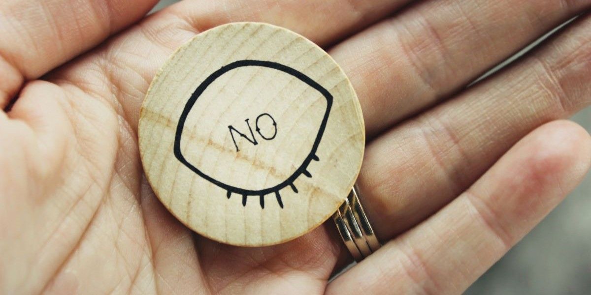 Hand holding a brown wood ornament that says NO