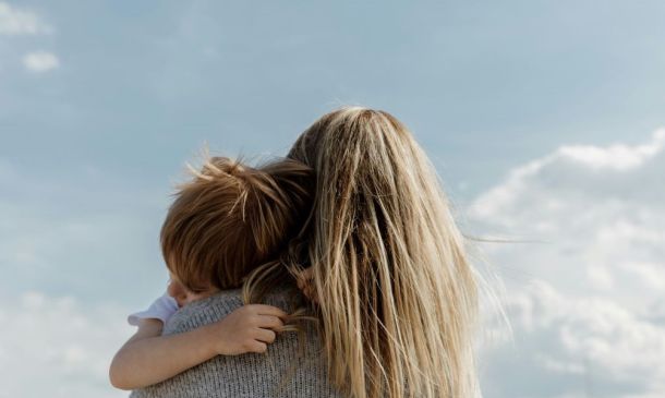 Photo from behind of a mother embracing a child and looking up toward the sky.