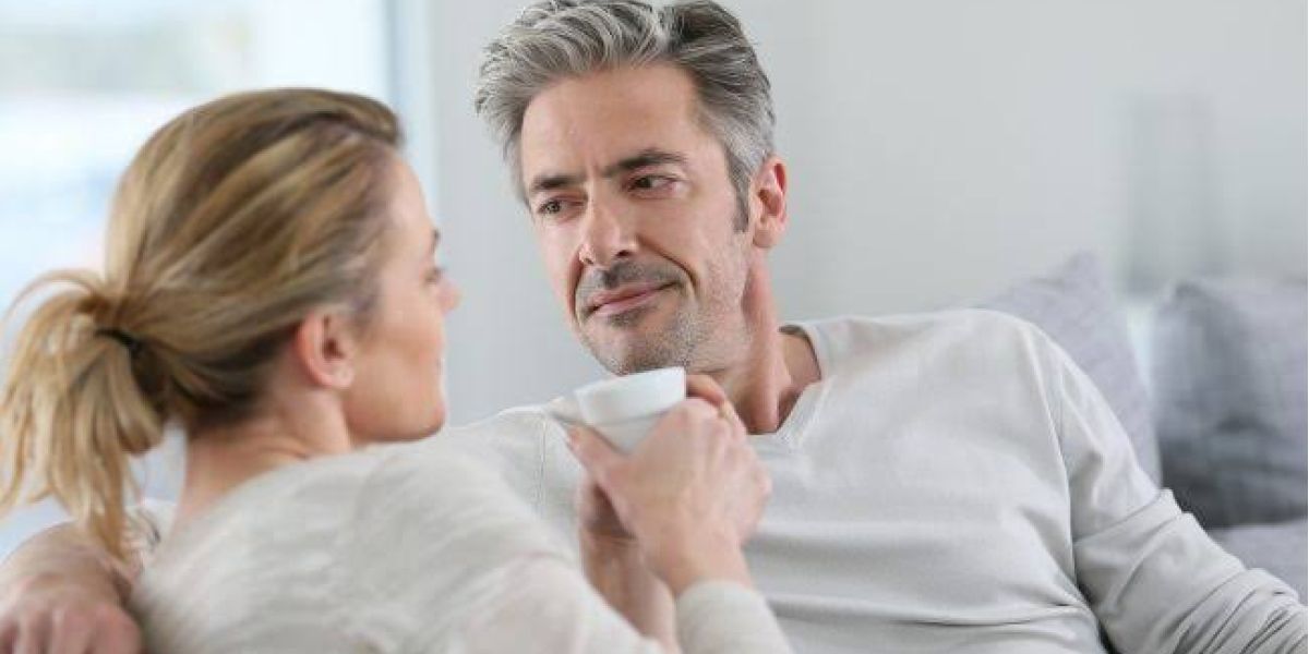 Middle aged couple sharing a coffee on the couch and having a conversation