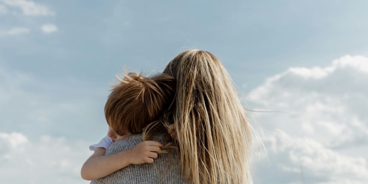 Photo from behind of a mother embracing a child and looking up toward the sky.